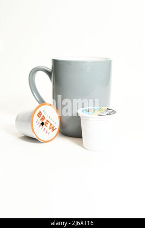 Graue Kaffeetasse und gebrauchte K-Tassen-Pads für eine Tasse, isoliert auf weißem Hintergrund Stockfoto