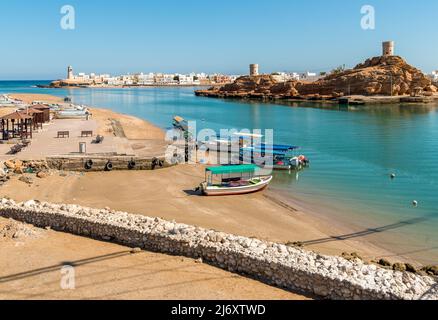 Blick auf die Bucht von Sur mit dem Leuchtturm Al Ayjah, Festungen auf den Felsen und traditionelle Fischerboote am Strand, Sultanat von Oman im Nahen Osten. Stockfoto