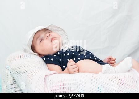 Schönes kaukasisches Baby, das friedlich auf einer kleinen Wiege schläft, gekleidet in einen blauen Kittel und einen weißen Hut. Auf einem weißen Hintergrund mit Platz zum Kopieren von Text Stockfoto