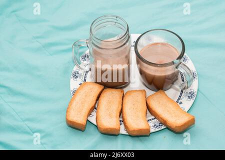 Frühstück für zwei Personen auf einem Teller mit Toast und zwei Tassen aus Klarglas mit Schokolade auf hellblauem Hintergrund. Leichter Snack für einen Cou Stockfoto