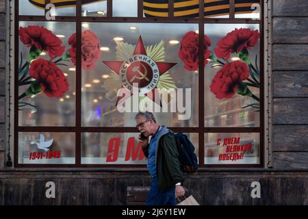 Moskau, Russland. 4.. Mai 2022. Ein Mann geht vor dem Hintergrund eines Schaufensters, das festlich für den Tag des Sieges (9.. Mai) geschmückt ist, auf der Straße des Gartenrings im Zentrum von Moskau, Russland Stockfoto