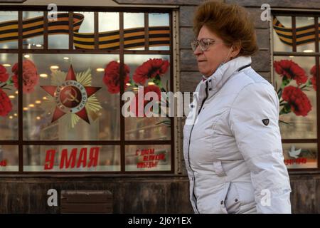 Moskau, Russland. 4.. Mai 2022. Eine Frau geht vor dem Hintergrund eines Schaufensters, das festlich für den Tag des Sieges (9.. Mai) geschmückt ist, auf der Straße des Gartenrings im Zentrum von Moskau, Russland Stockfoto