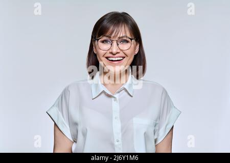 Headshot Porträt von lächelnden schönen mittleren Alters Frau, positive Frau in Brille im Hemd Blick auf die Kamera auf hellen Studio-Hintergrund. Emotionen, Stockfoto