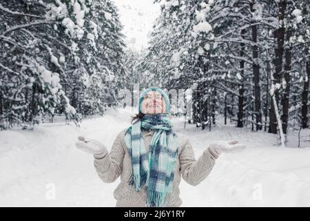 Ein Mädchen steht im Winterwald, wirft fröhlich den Schnee in weißen Fäustlingen auf Stockfoto