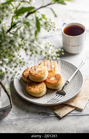 Syrniki – traditionelle russische Käsepfannkuchen, die zum Frühstück auf grauem Hintergrund serviert werden Stockfoto