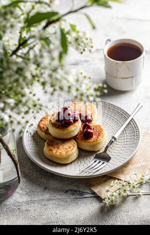 Syrniki – traditionelle russische Käsepfannkuchen, die zum Frühstück mit Kirsche serviert werden Stockfoto