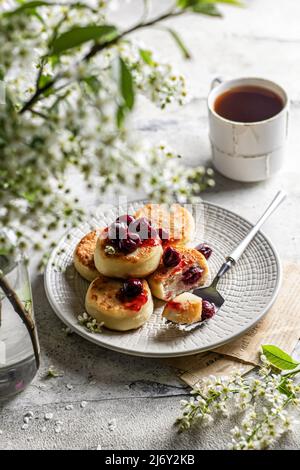 Syrniki – traditionelle russische Käsepfannkuchen, die zum Frühstück mit Kirsche serviert werden Stockfoto