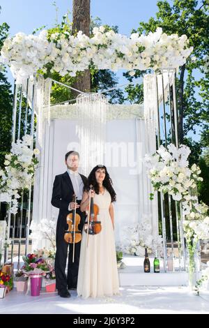 Mann und Frau Geiger auf Hochzeit Bogen Hintergrund. Stockfoto