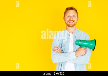 Rothaariger junger Mann mit einem Megaphon, das isoliert auf gelbem Hintergrund steht Stockfoto