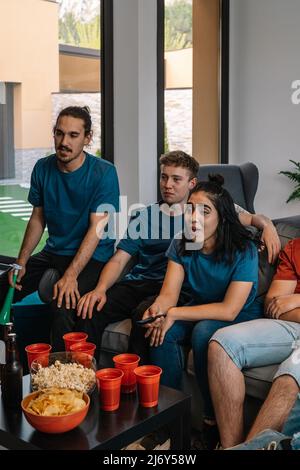 Freunde genießen zusammen ein Sportspiel im Fernsehen. Einen Film ansehen. Jugendliche essen und trinken. Stockfoto