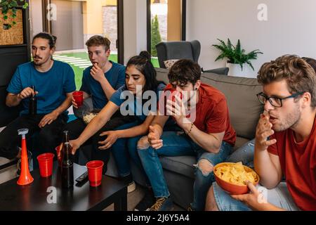Freunde, Hausfeier Fernsehen. Gruppe, die einen Film oder eine Sportveranstaltung. Junge Menschen essen und trinken. Stockfoto