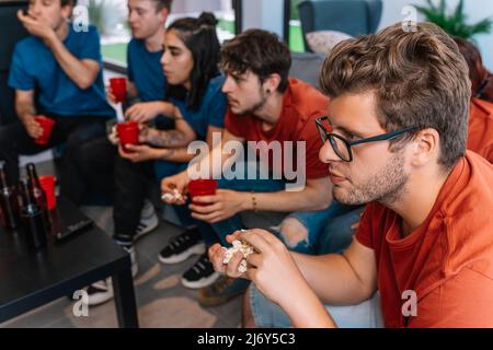 Freunde, die erwartungsvoll auf den möglichen Sieg ihrer Sportmannschaft schauen. Gruppe, die einen Film oder eine Sportveranstaltung im Fernsehen ansieht. Stockfoto