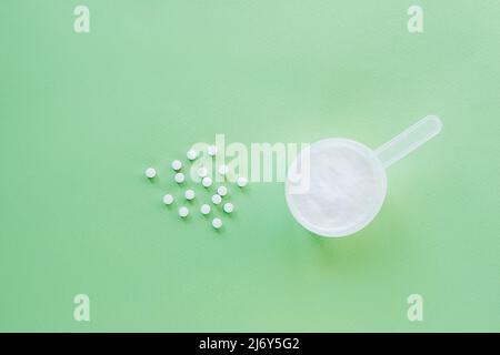 Kollagenpulver und Vitamin C-Tabletten auf grünem Hintergrund. Nahrungsergänzungsmittel zur Unterstützung der Kollagenproduktion. Draufsicht, flach liegend, Kopierbereich. Stockfoto