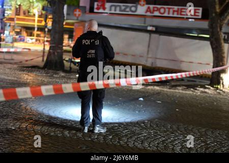 04. Mai 2022, Nordrhein-Westfalen, Duisburg: Ein Polizeibeamter sucht nachts auf dem Hamborner Altmarkt in Marxloh nach Spuren der Schüsse. Bei einer Auseinandersetzung mit Schusswaffen in Duisburg sind am Mittwochabend vier Personen verletzt worden. Foto: Roberto Pfeil/dpa Stockfoto