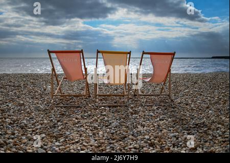 Drei Liegestühle am britischen Kiesstrand an der Küste mit Blick auf das Meer. Stockfoto