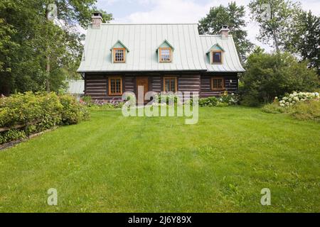 Altes Blockhaus im kanadischen Stil aus dem Jahr 1800s mit landschaftlich gestaltetem Vorgarten im Sommer. Stockfoto