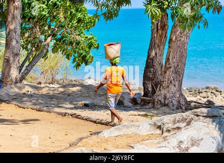 Frau, die mit einem Korb auf dem Kopf an einem Strand in Madagaskar zum Markt läuft Stockfoto