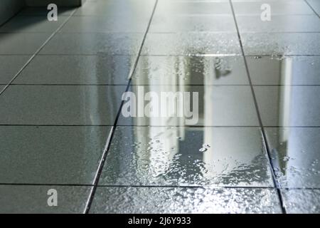 Eine große Pfütze auf dem Fliesenboden wurde durch Wasser von der Decke infolge eines Dachlecks oder einer platzten Wasserleitung verursacht, selektiver Fokus Stockfoto