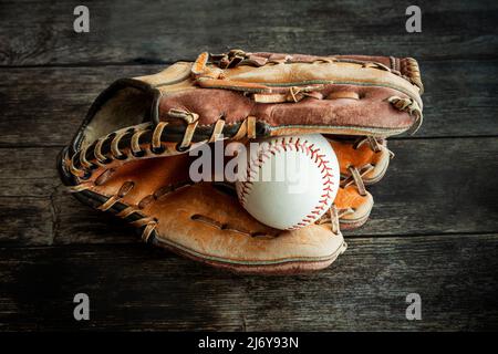 Leder-Baseballhandschuh oder Softballhandschuh mit Ball auf rustikalem Holzhintergrund. Stockfoto