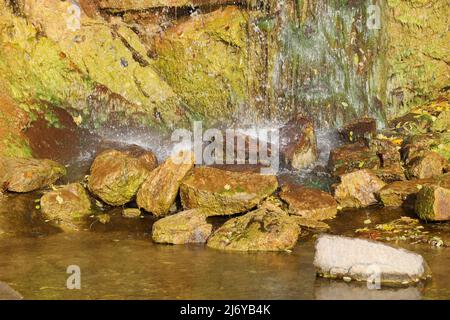 Wasserfall zwischen Steinen und Bäumen. Nahaufnahme von Felsbrocken im Wasser. Riesige Steine in grünem Moos. Schöne Landschaft von schnellen Wasserfall mit kleinen Whirlpool Stockfoto