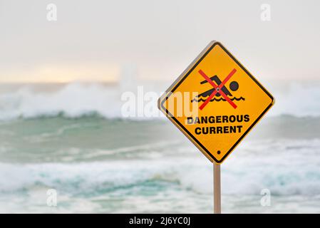 März 2022:Ein gefährliches Stromschild am Bronte Beach in Sydney, Australien an einem Wochenende voller wilder Brandung und Nebel am frühen Morgen, die einen grauen Hintergrund erzeugen Stockfoto