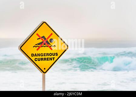 März 2022:Ein gefährliches Stromschild am Bronte Beach in Sydney, Australien an einem Wochenende voller wilder Brandung und Nebel am frühen Morgen, die einen grauen Hintergrund erzeugen Stockfoto