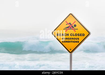 März 2022:Ein Warnschild am Bronte Beach in Sydney, Australien, an einem Wochenende voller wilder Brandung und Nebel am frühen Morgen, die einen grauen Hintergrund erzeugen Stockfoto