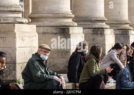 Bild eines weißen kaukasischen älteren Mannes in Bordeaux, Frankreich, der auf einer Treppe inmitten einer Menschenmenge sitzt, während er während des eine Atemmaske trägt Stockfoto