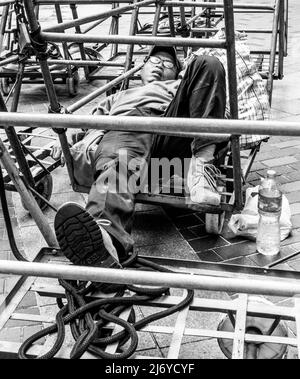 Ein Arbeiter macht eine Pause und schläft auf Trolleys in einer Hong Kong Street. Stockfoto