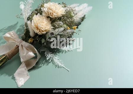 Bouquet von getrockneten Blumen auf grünem Hintergrund platziert. Konzept für Hochzeit und Feier. Stockfoto