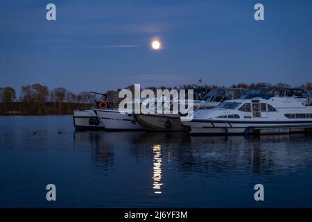 Vollmond leuchtet hell auf Booten und Yachten im Hafen. Nacht am See in einer ländlichen Gegend. Ruhige Szene mit schöner Natur. Landschaft Stockfoto