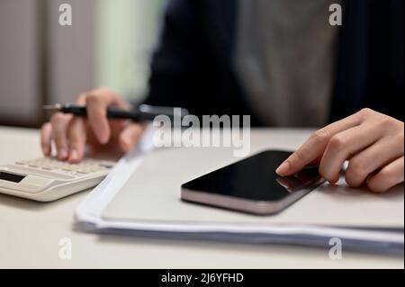 Nahaufnahme, weibliche Hände tippen auf dem Handy-Bildschirm und verwenden Taschenrechner, um ihre Finanzarbeit zu überprüfen. Stockfoto