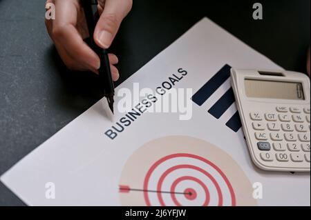 Aus nächster Nähe zeigen Geschäftsleute mit einem Stift auf die Geschäftsziele, die den Plan zum Bericht vorlegen. Stockfoto