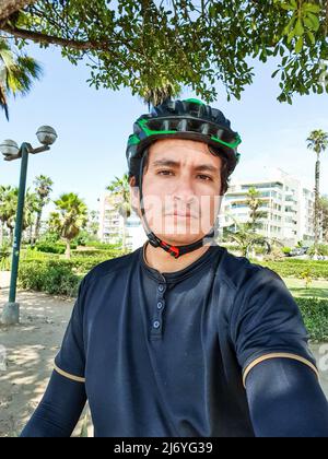 Junger hübscher Radfahrer in schwarzer Radsportkleidung, der einen Helm in einem Park trägt Stockfoto