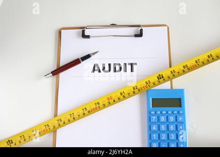 Audit-Wort auf Arbeitspapier mit Stift, Maßband und Rechner. Geschäftsverbesserungskonzept. Isolierter Hintergrund. Stockfoto