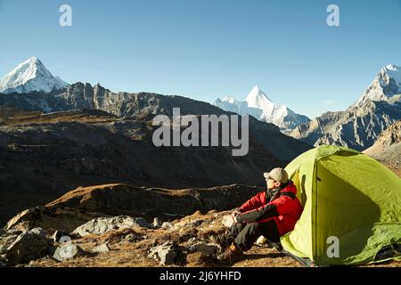 asiatischer Mann, männlicher Camper, der im Zelt sitzt und die Morgensonne im yading Nationalpark, Bezirk daocheng, Provinz sichuan, china genießt Stockfoto