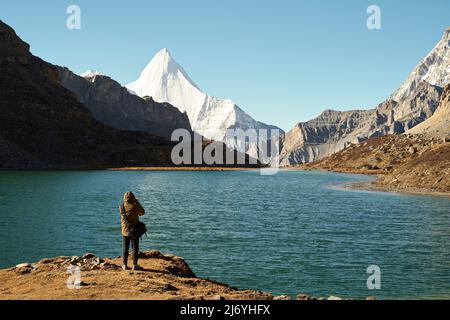 Rückansicht eines asiatischen Fotografen, der ein Foto vom heiligen Berg jampayang und dem See boyongcuo im yading Nationalpark, Landkreis daocheng, sichuan pro, macht Stockfoto