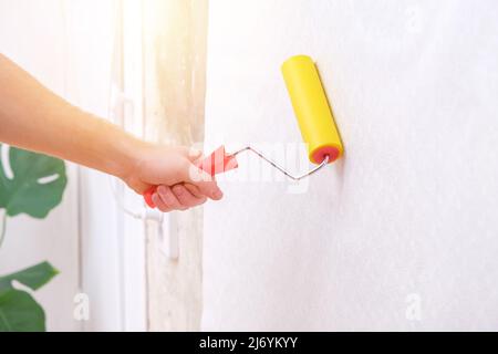 Ein Mann rollt eine Leinwand aus weißer Tapete mit einer Nahttapete gelbe Rolle. Luftblasen und Kleber unter der Tapete entfernen. Tapezieren. Die Reparatur des Zimmers, der Wohnung, des Hauses. Stockfoto