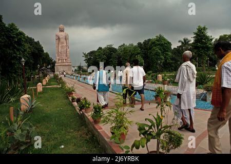 Besucher, die zu einer 80 Meter hohen Sandsteinstatue des stehenden Buddha in Sarnath am Stadtrand von Varanasi, Uttar Pradesh, Indien, wandern. Die von 1997 bis 2011 erbaute Statue war das Ergebnis einer gemeinsamen Anstrengung Thailands und Indiens. Stockfoto