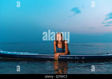 Sommersport. Porträt von jungen lächelnden gebräunten Frau Posen lehnt auf einem Brett. Speicherplatz kopieren. Konzept des Surfens. Stockfoto