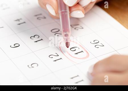 Weibliche Handmarkierung mit einem roten Stift auf einem Kalender umkreist den Tag, Deadline-Konzept Stockfoto