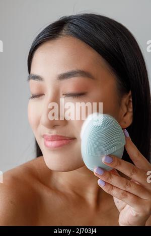 Lächelnde asiatische Frau, die im Studio ein Gesichtsmassager verwendet Stockfoto