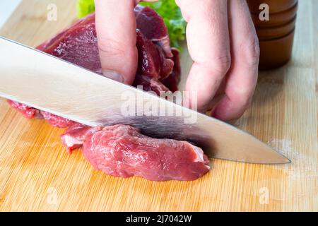 Nahaufnahme eines Küchenchefs, der rohes Rindfleisch mit einem Messer in einer Küche schneidet Stockfoto