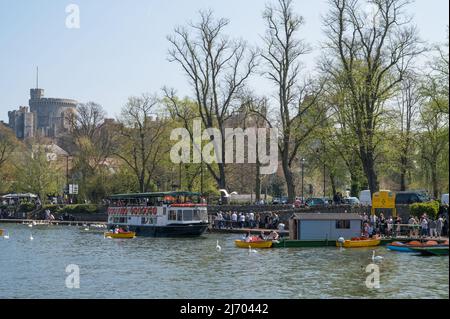 Menschen, die einen sonnigen Frühlingstag auf dem Flussweg der Themse genießen und Motorboote mieten. Windsor Castle im Hintergrund. England, Großbritannien. Stockfoto