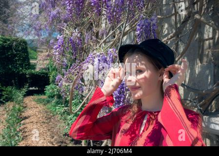 Die hübsche junge Frau steht neben der Glyzinie. Mädchen genießen Frühling Zeit. Outfit für den Frühling. Stockfoto