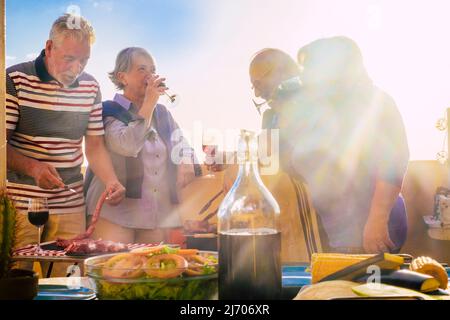 Freunde alter Leute genießen zusammen mit Essen und Getränken die Freizeit. Grill bbq Aktivität mit zwei fröhlichen Paare von erwachsenen Männern und Frauen h Stockfoto