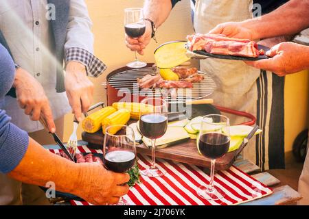 Nahaufnahme einer Gruppe von Freunden, die Essen und Wein von einem Tisch nehmen. Grillen Sie Ihre Freizeit im Freien mit Männern und Frauen, die Spaß haben und ho genießen Stockfoto