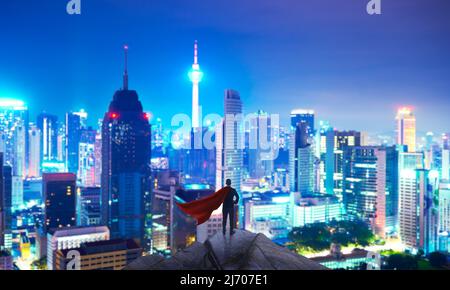 Geschäftsmann in Anzug und Umhang Held stehen oben mit Blick auf die Stadt und denken Business-Plan der Zukunft . Nachtaufnahme . Stockfoto