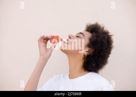 Glückliche afroamerikanische junge Frau, die Gelee-Bubble-Klebeband auf Weiß isst Stockfoto