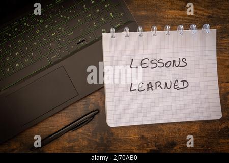 Laptop, Stift und Notizbuch mit Text Lessons learned on wooden table. Konzept von Business und Technologie Stockfoto